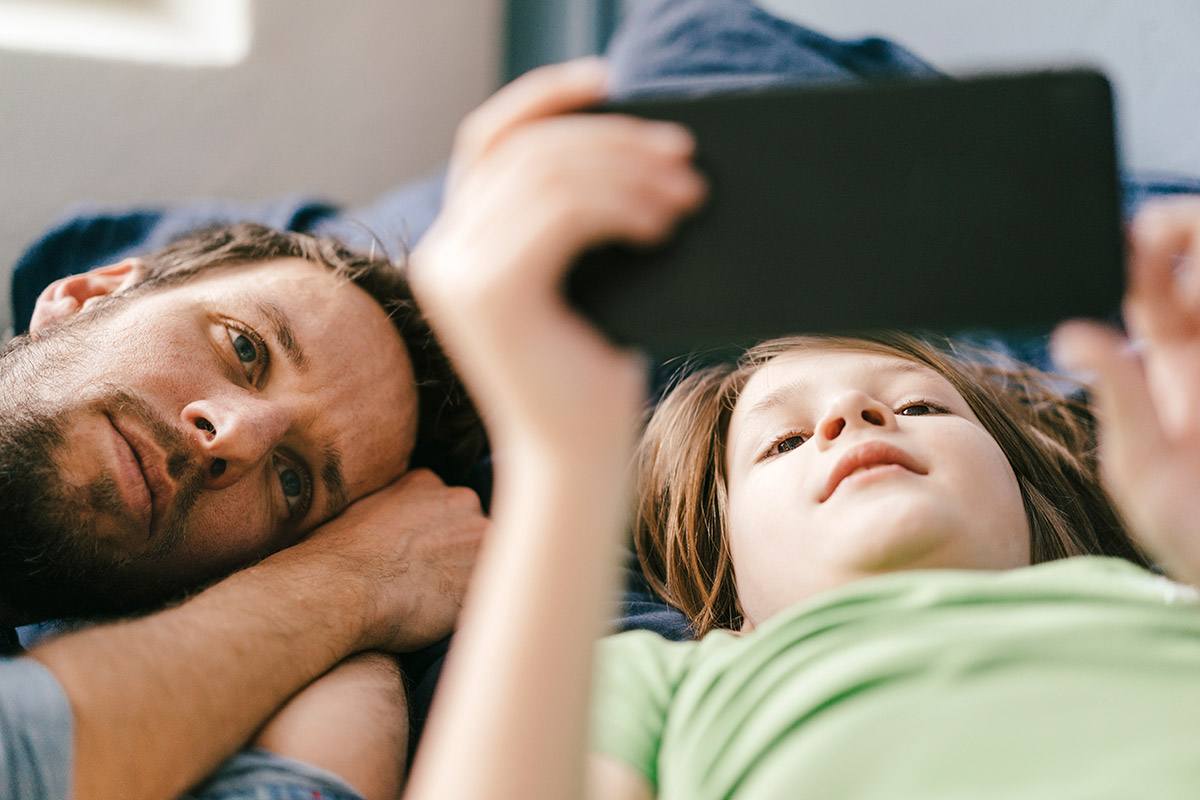 En pappa och sin son som kollar på en mobiltelefon tillsammans i soffan.
