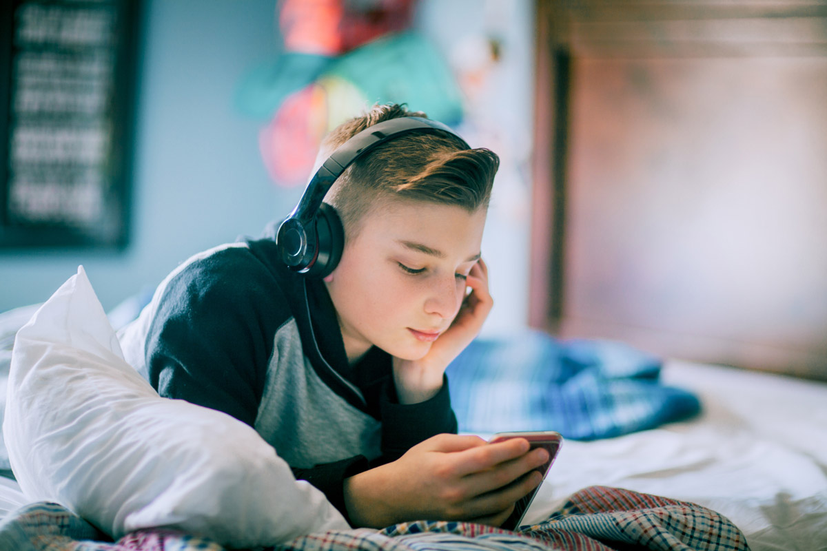 Bild på en ensam tonåring som ligger i sängen och tittar film på mobilen