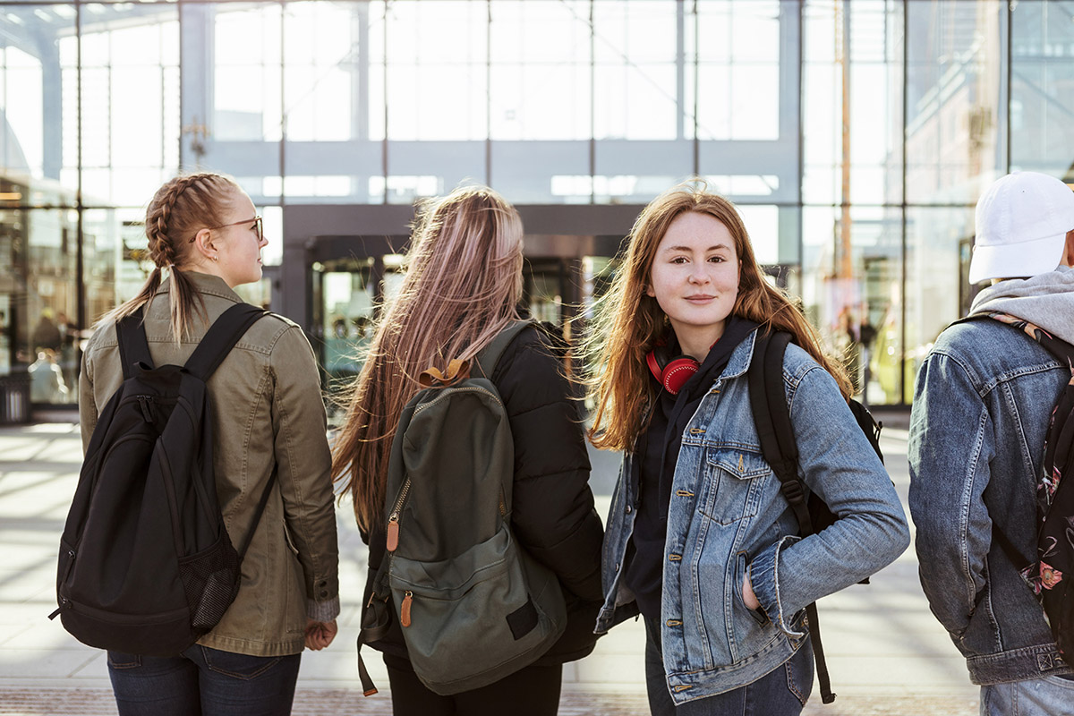 Bild på fyra ungdomar utanför ett stationshus där en vänder sig mot kameran