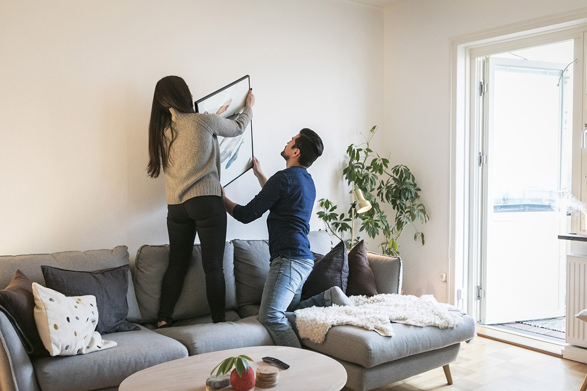 Bild på två personer som hänger upp en tavla ovanför en soffa i ett vardagsrum