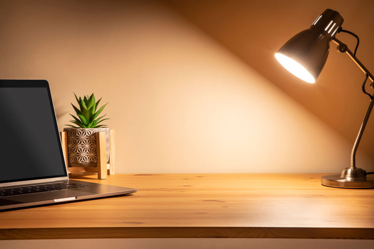 En tänd skrivbordslampa bredvid en laptop